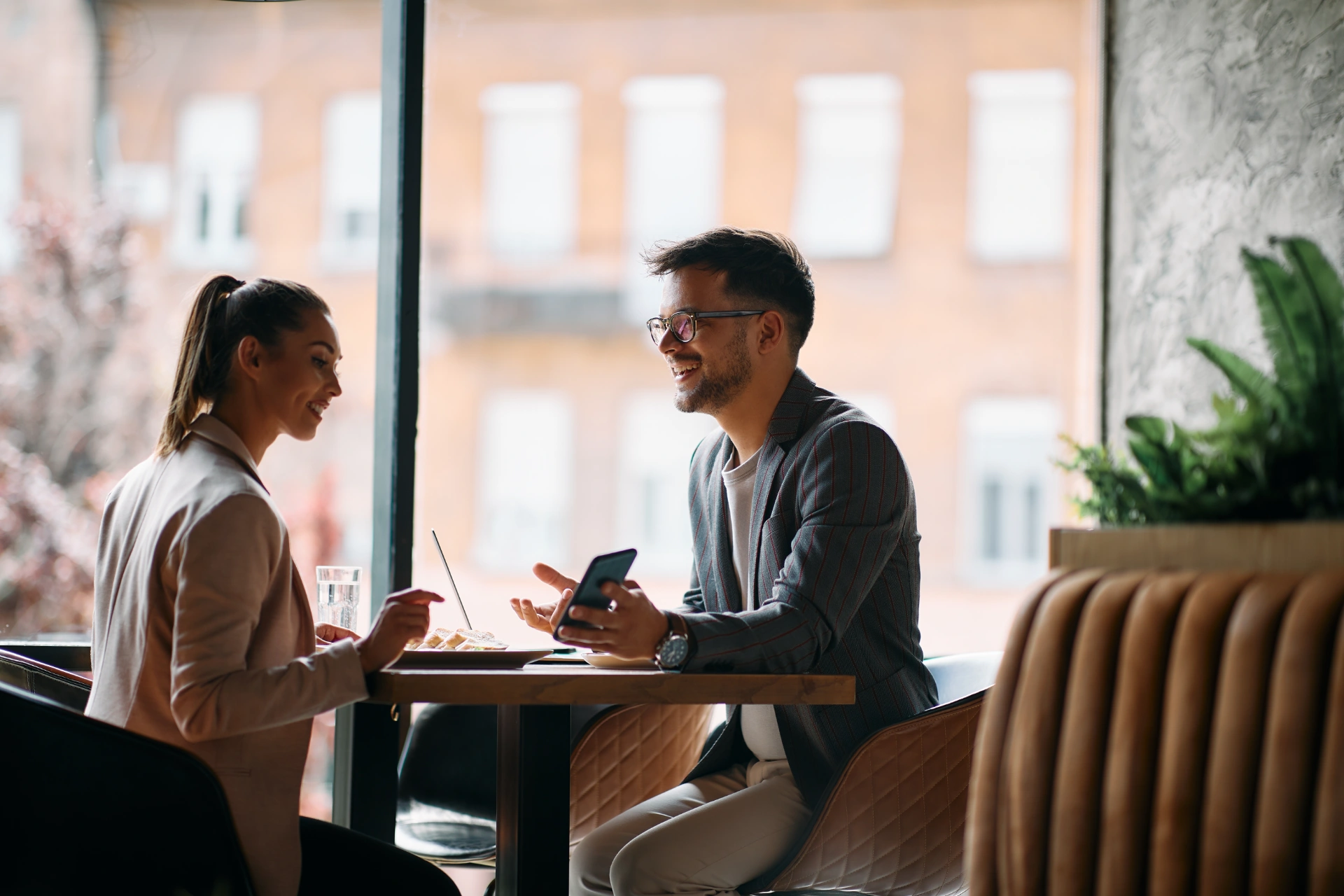 Happy businessman showing something on smart phone to female colleague during their breakfast in a cafe.